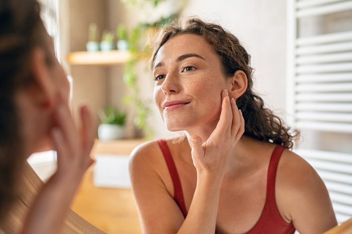 Young woman checking her skin in the mirror in the morning