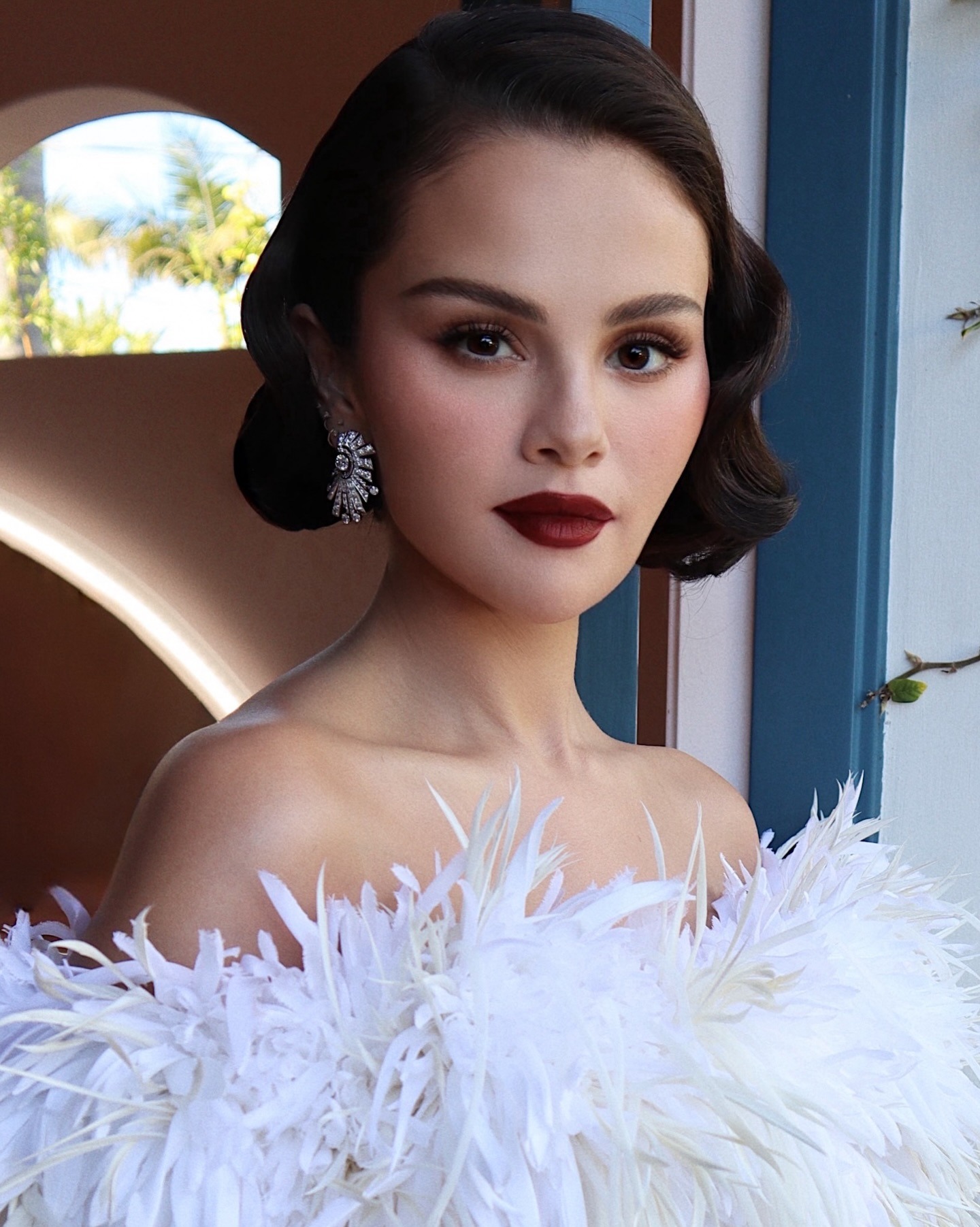 An image of Selena Gomez wearing deep red lipstick and neutral, Old Hollywood glam makeup.