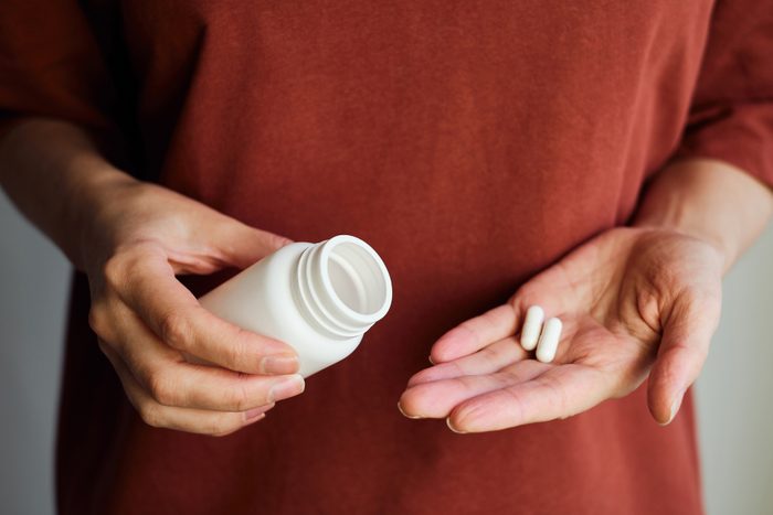 A woman pours pills or vitamins from a jar onto her hand.