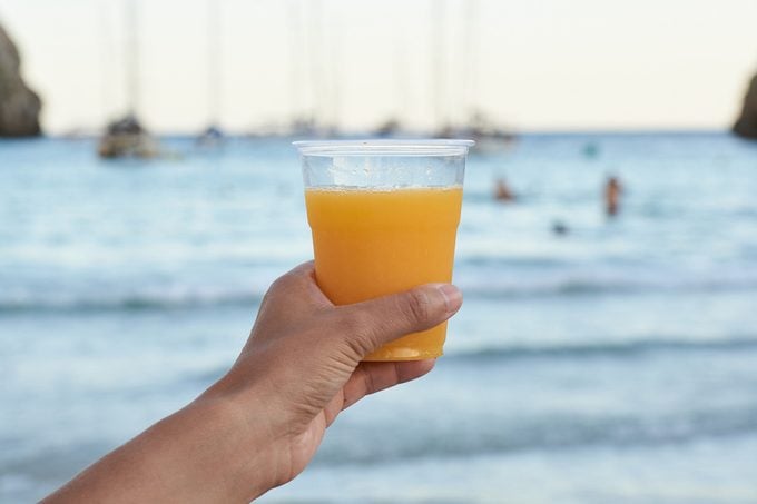 a hand holding a glass of orange juice with a marina in the background
