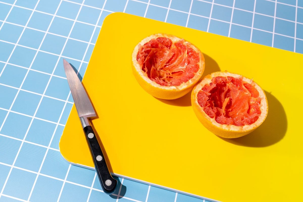 Two Grapefruit Halves On A Cutting Board And A Knife On Blue Background