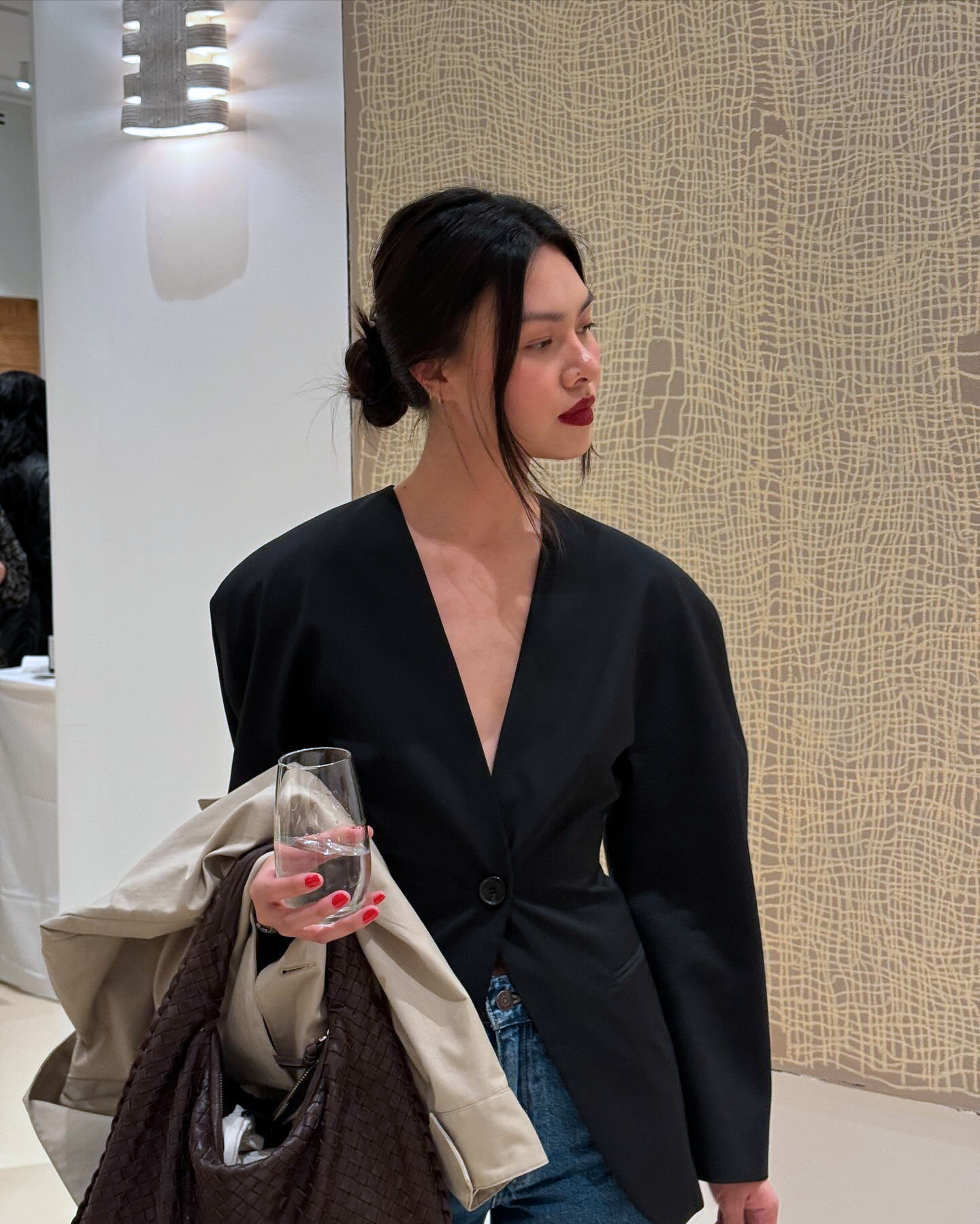 NYC style influencer Minim Nguyen poses with a low bun, red lipstick, waisted blazer, jeans, and a brown woven bag
