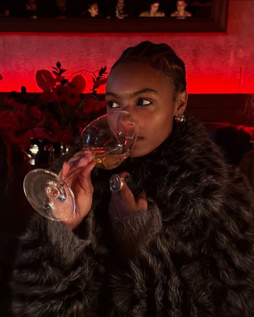 An image of a woman drinking wine in a restaurant wearing a fur coat.