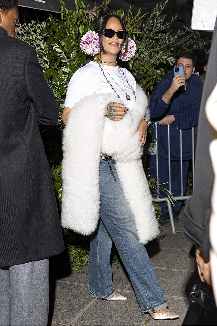 Rihanna wearing pink earmuffs, a white t-shirt, blue jeans, a white scarf, and pink satin heels