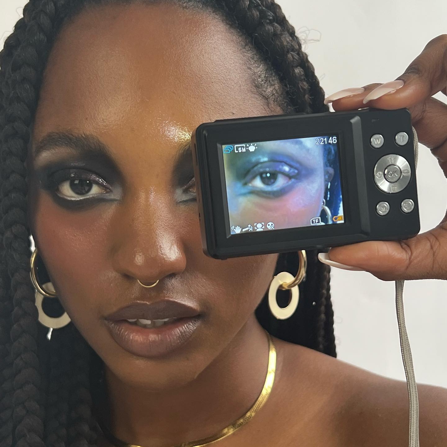 A woman with bold makeup holding a digital camera in front of her eye.