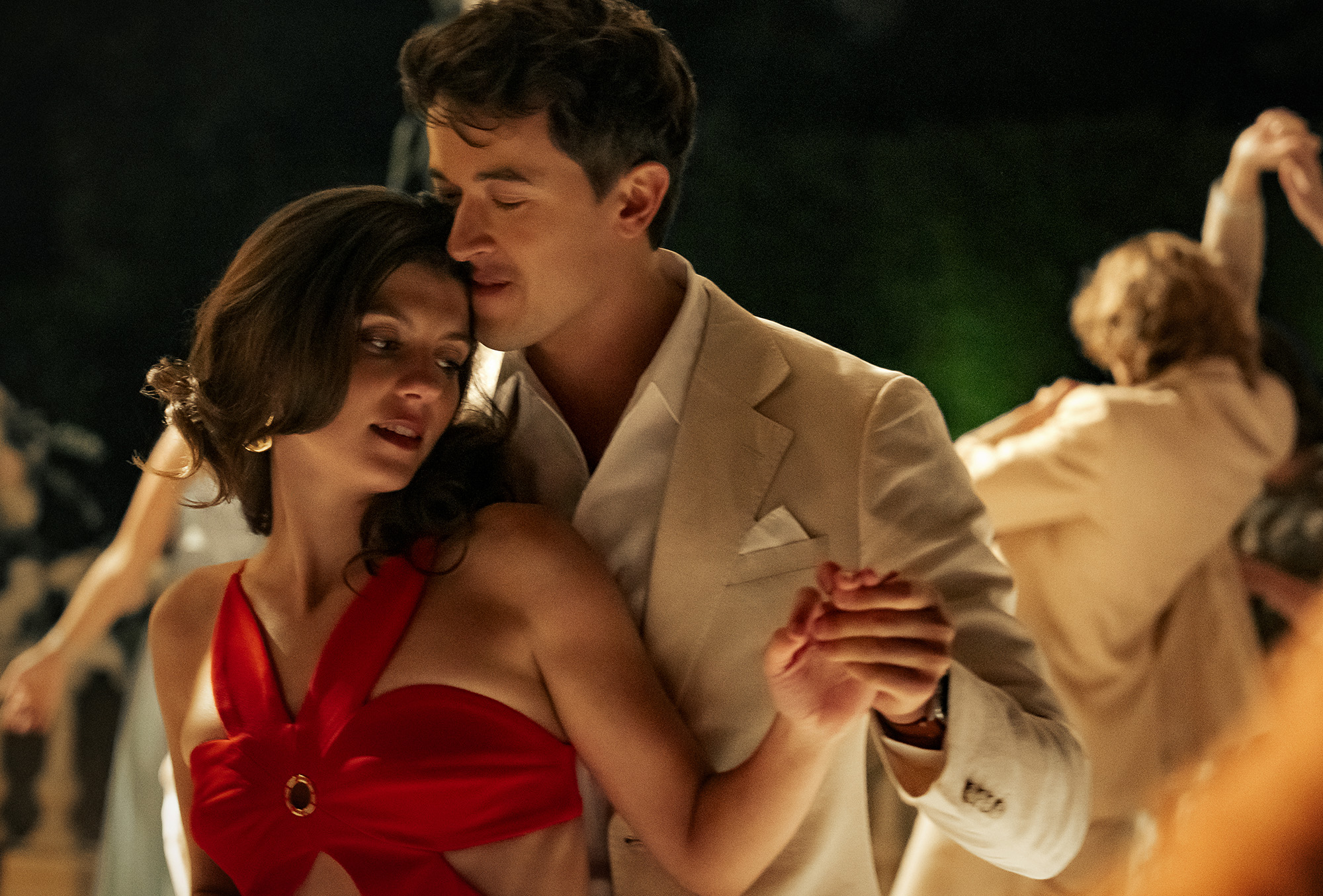 Film still from People We Meet on Vacation featuring characters Poppy and Alex played by Emily Bader and Tom Blythe. They are dancing at a wedding and she is wearing a red cutout dress and he is wearing a tan suit.