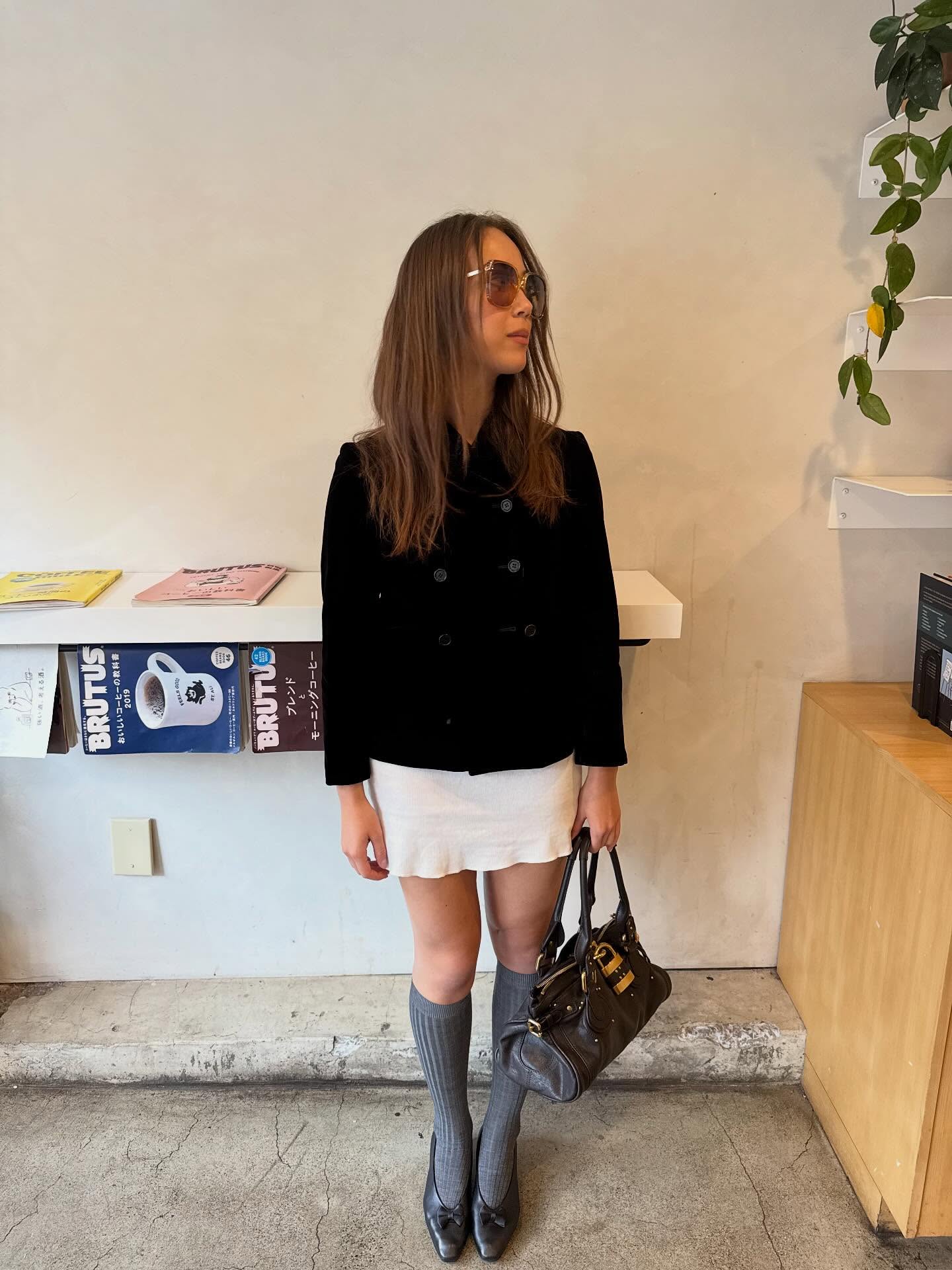 Laufey is wearing a double-breasted coat, a white mini skirt, knee-high grey socks, pumps, and a Chlo&eacute; Paddington bag