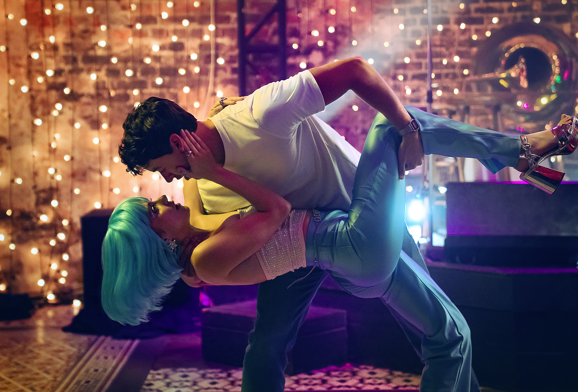 Film still from People We Meet on Vacation featuring characters Poppy and Alex played by Emily Bader and Tom Blythe. The characters are dancing and Poppy is wearing a blue wig.