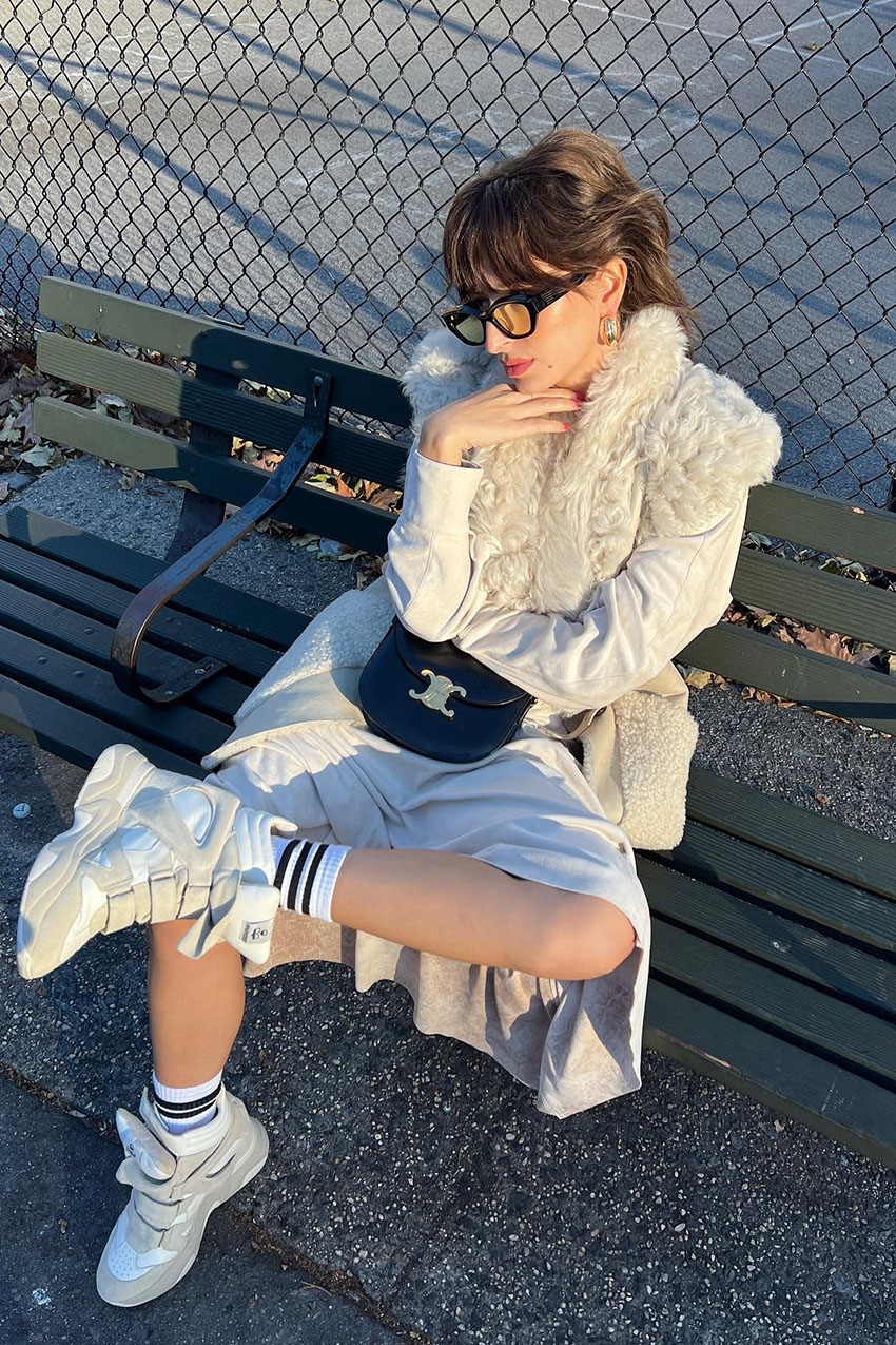 a woman wearing a white fur jacket, white skirt, and wedge sneakers