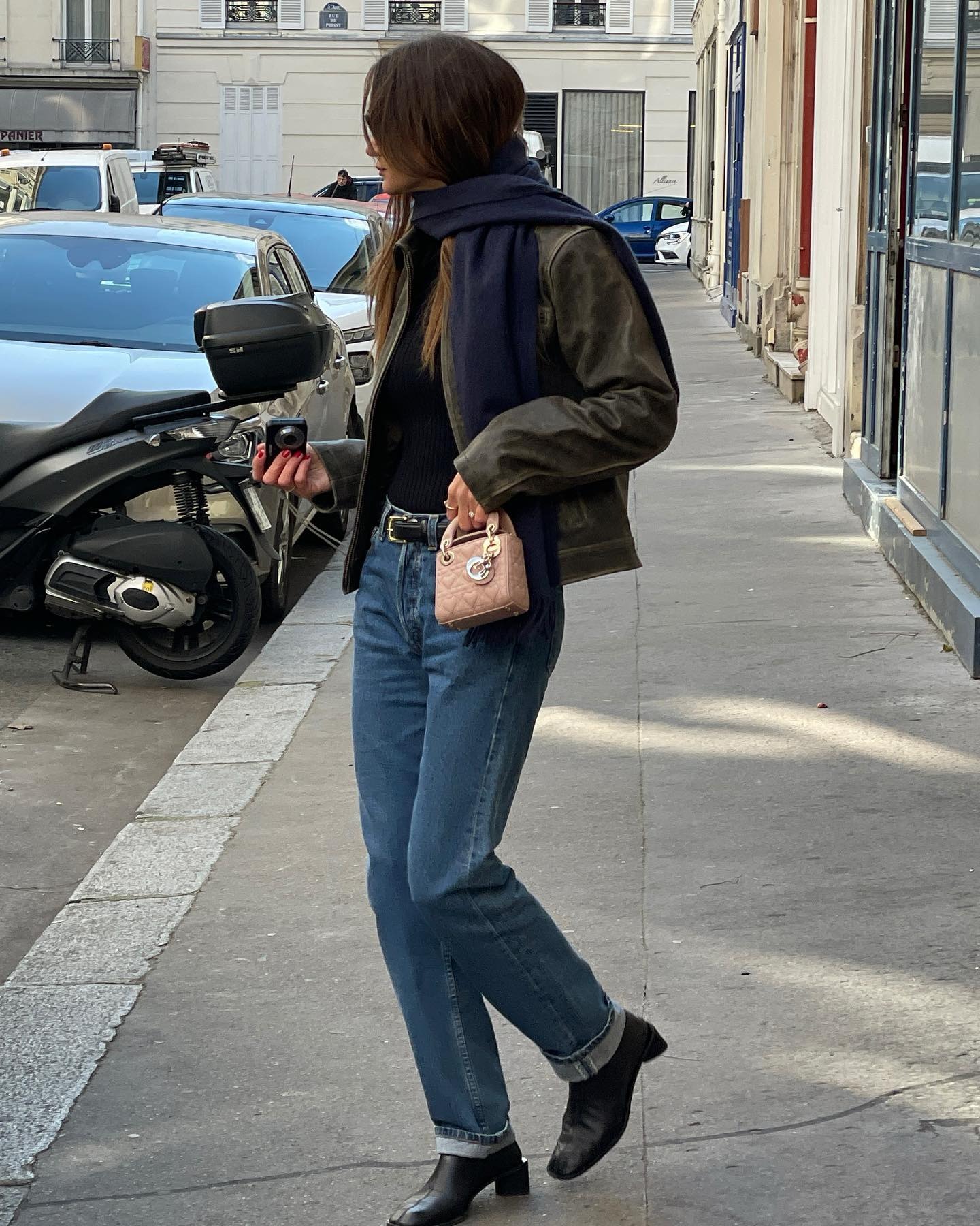 Anne Laure Mais wears cuffed jeans, black ankle boots, a Dior pink bag, a navy scarf, and a leather jacket.