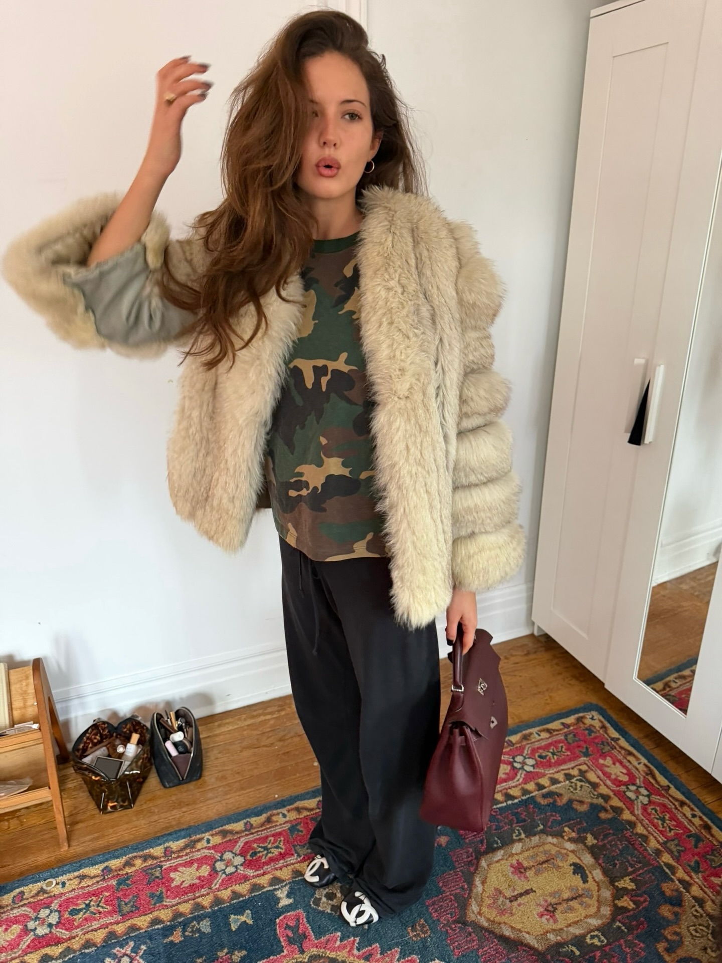 Ruby Lyn is wearing a pair of black sweatpants, Chanel Cambon ballet flats, a camo shirt, a fur coat, and red bag