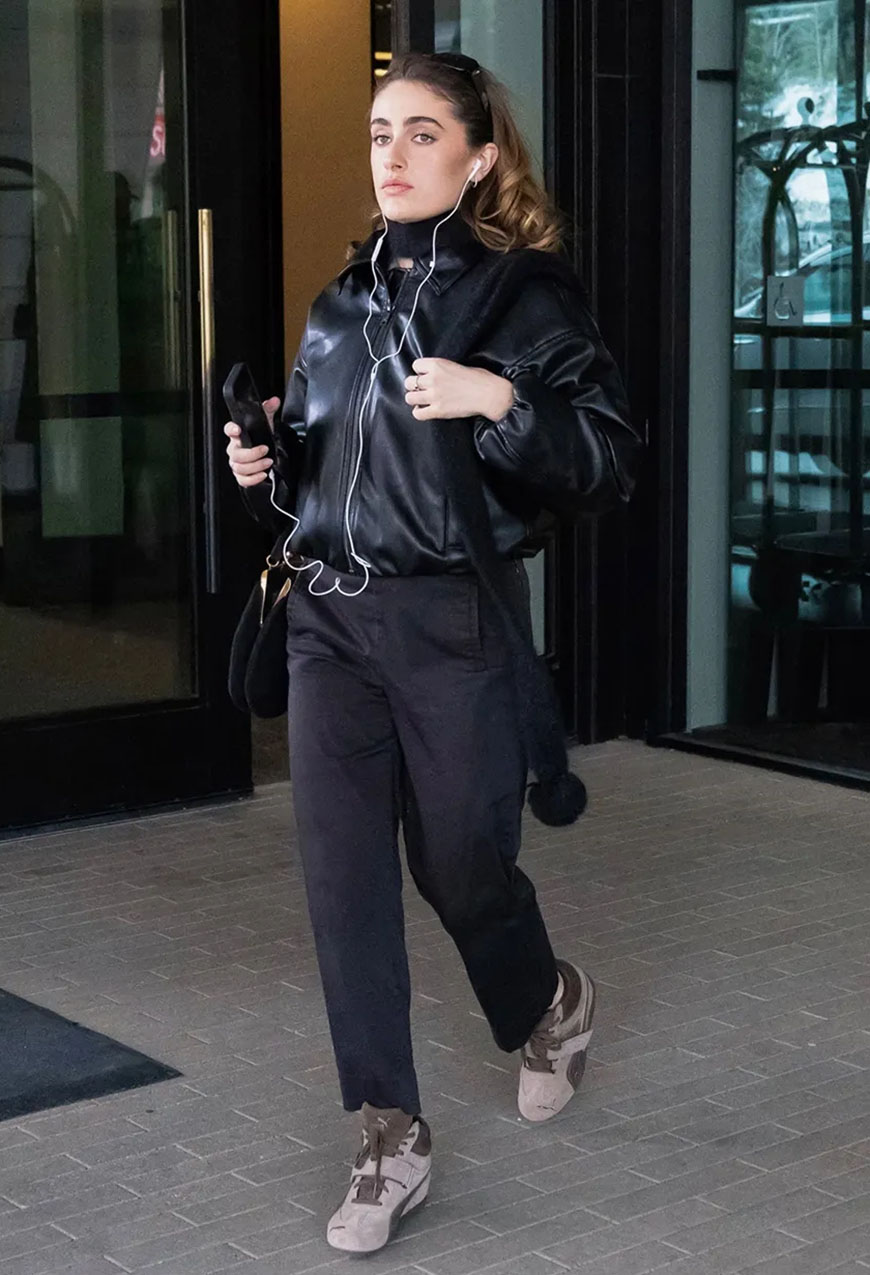 Rachel Sennott wearing a black leather jacket, black pants, and wedge sneakers