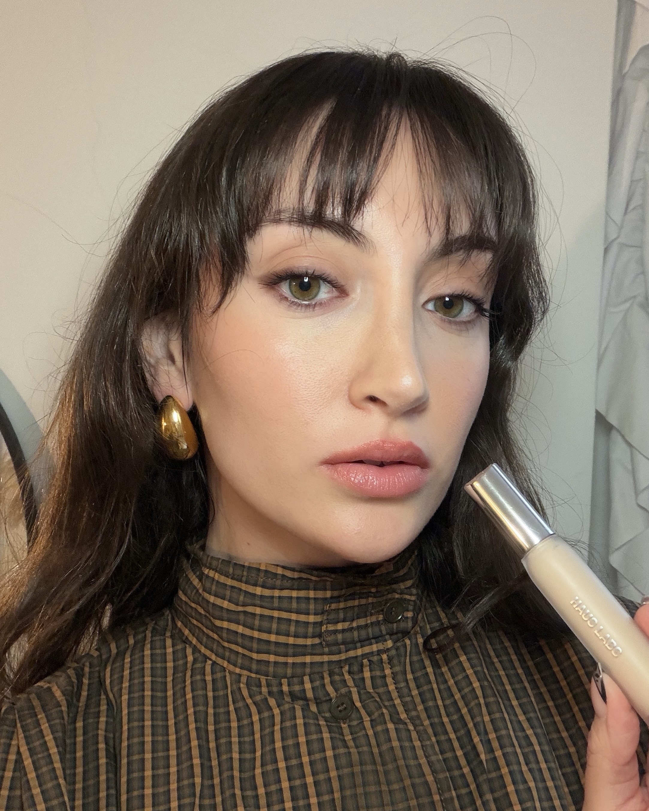 An image of Who What Wear associate beauty editor Alyssa Brascia wearing and holding the Haus Labs Triclone Skin Tech Concealer.