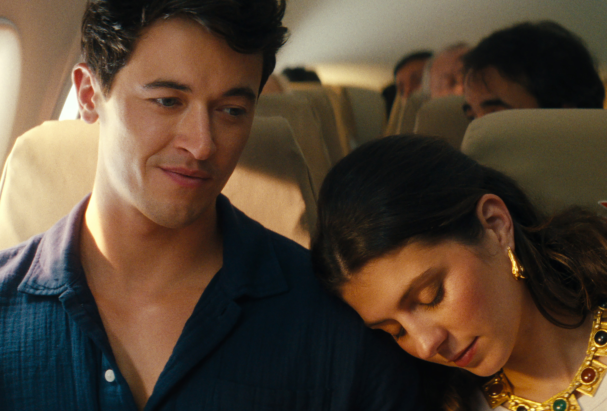 Film still from People We Meet on Vacation featuring characters Alex and Poppy on an airplane. Poppy is leaning on Alex's shoulder.