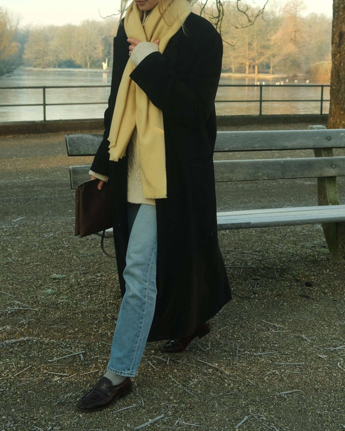 Anouk wears a yellow scarf, black coat, stovepipe jeans, and loafers.